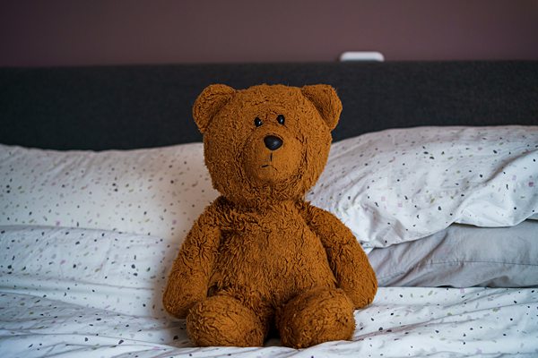 Teddy bear sitting on a bed with white sheets.