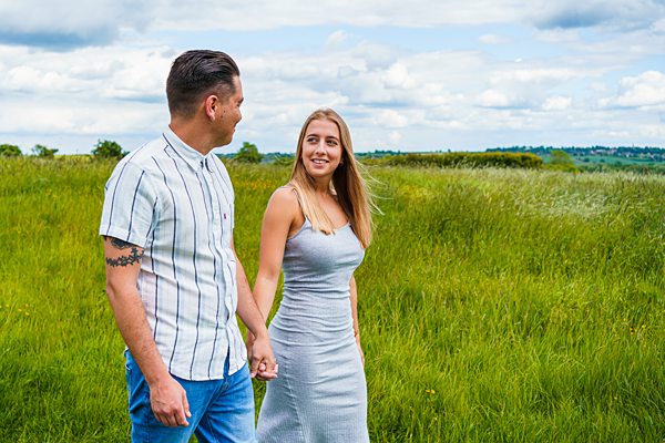 Couple walking hand-in-hand through a green field.