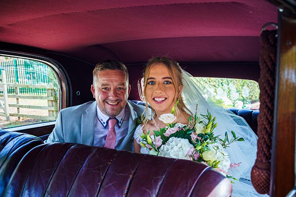 Bride and father smiling in vintage wedding car