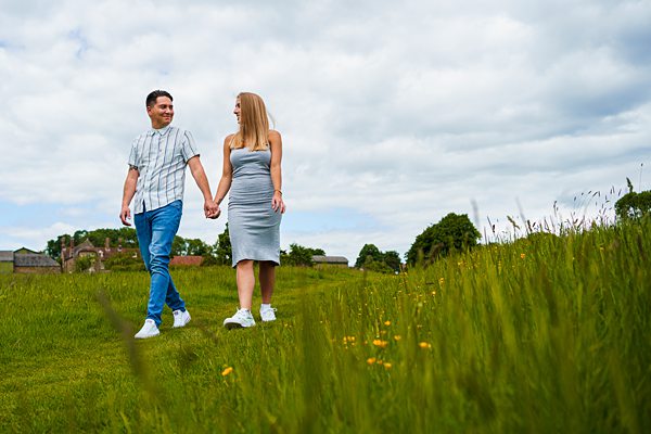 Couple holding hands, walking through green field.