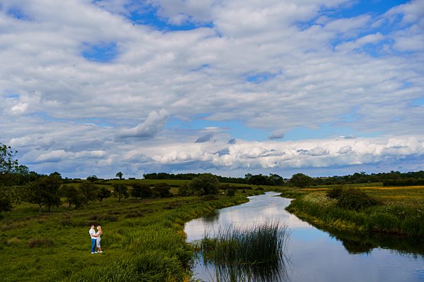 Couple by serene river under cloudy sky in countryside.