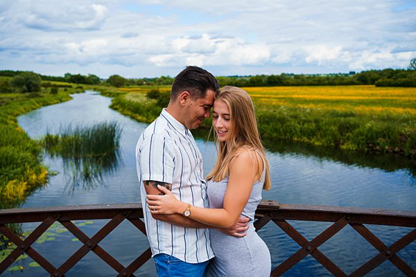 Couple embracing on bridge over scenic river.