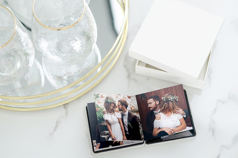Wedding photo album on marble table with glasses.