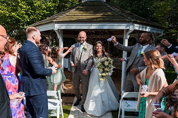 Newlyweds with guests throwing confetti at garden wedding.