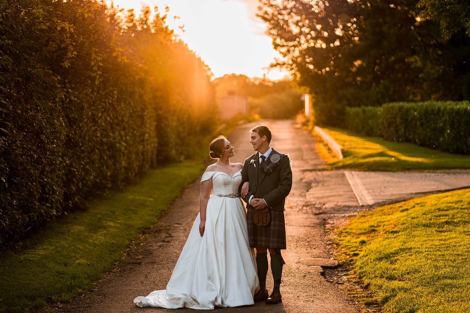 Couple in wedding attire smiling at sunset.