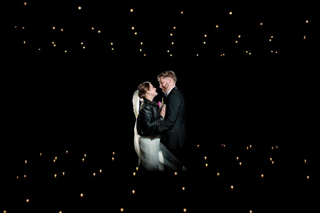 Couple embracing at night with twinkling lights background.