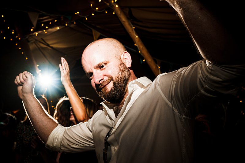 Man dancing at festive event with string lights.