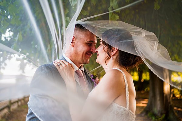 Bride and groom sharing moment under veil outdoors