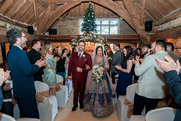 Couple at wedding ceremony receiving applause in barn venue.