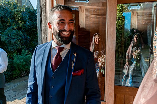 Man in suit smiles with women reflecting in door glass.