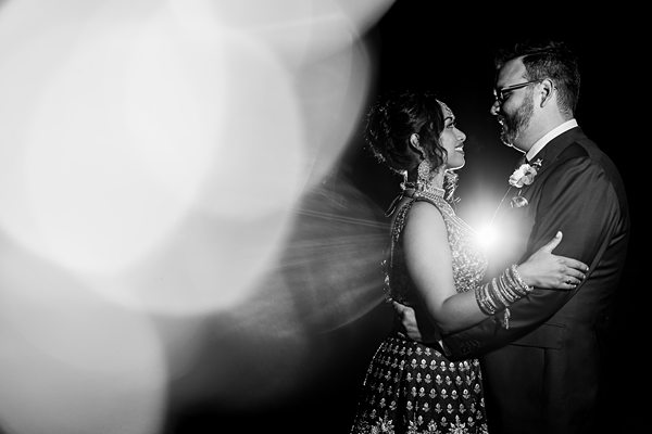 Couple embracing in elegant attire with dramatic backlighting