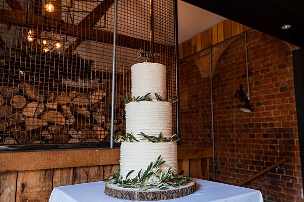 Three-tier wedding cake with olive leaves on rustic stand.