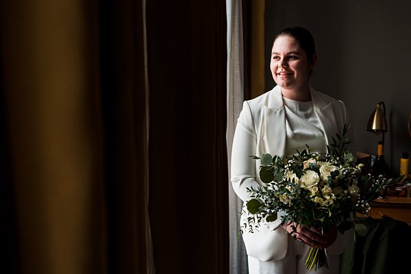 Bride in white suit holding bouquet.
