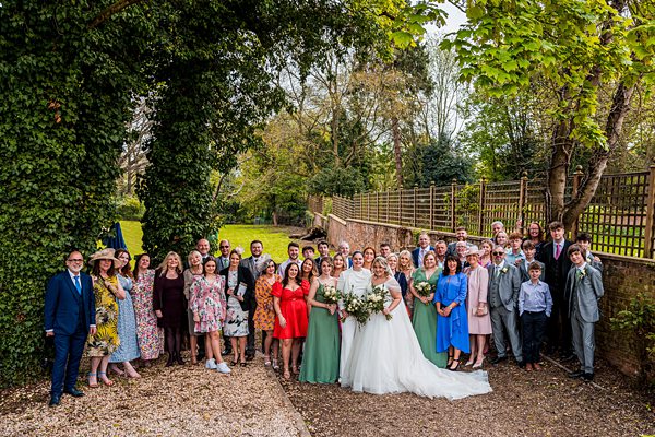 Outdoor wedding group photo with smiling guests.