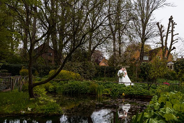 Bride kissing groom by pond in lush garden setting