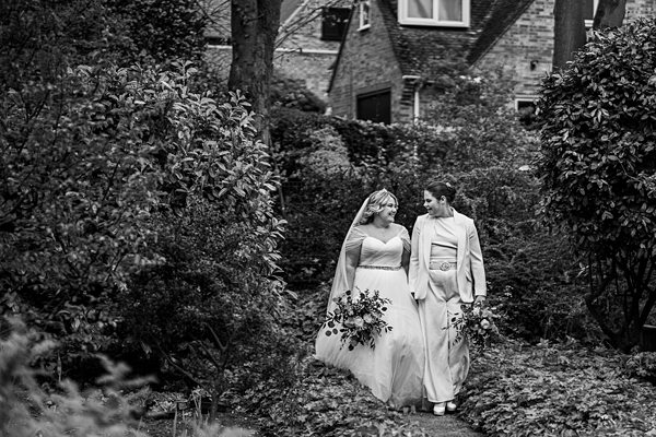 Couple in wedding attire walking through garden.
