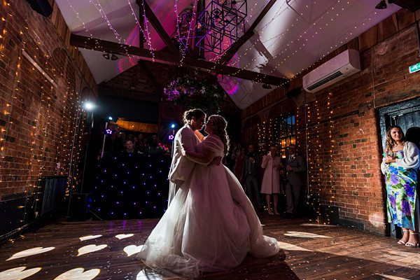 Couple dancing at rustic wedding venue with fairy lights.