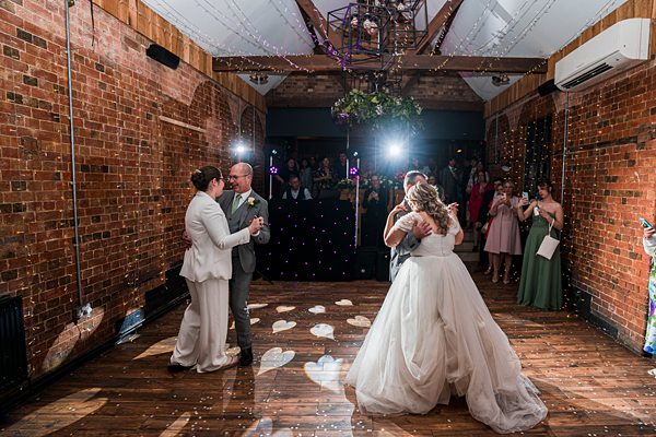Couples dancing at rustic brick-walled wedding reception.