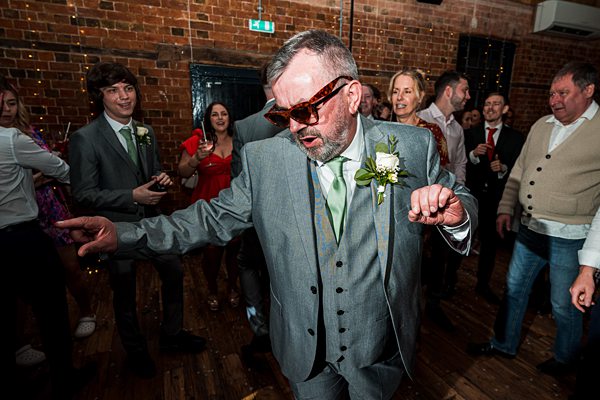 Man dancing at wedding reception, guests watching.