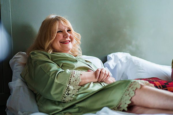 Smiling woman relaxing on bed in green robe.