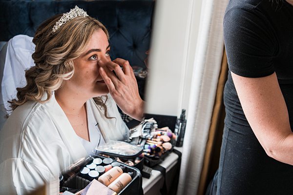 Bride applying makeup on wedding day.