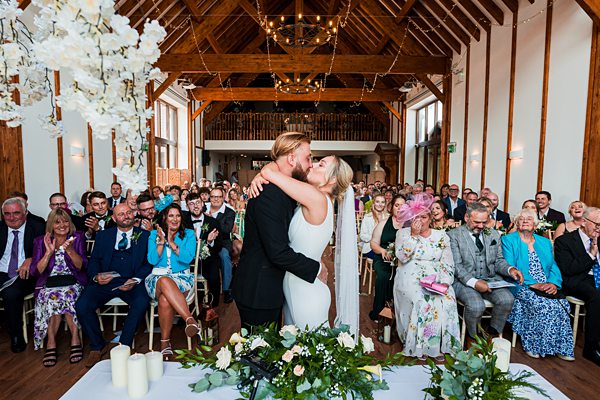 Couple kissing at wedding ceremony with guests watching.