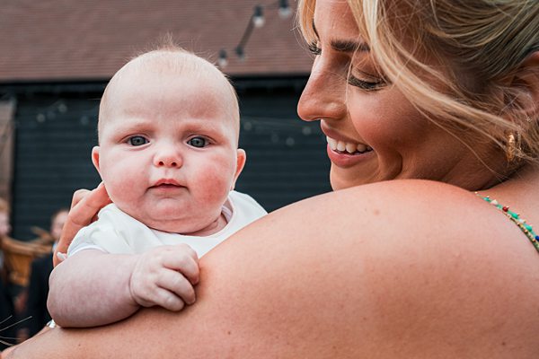 Woman holding baby outside, both looking at camera.