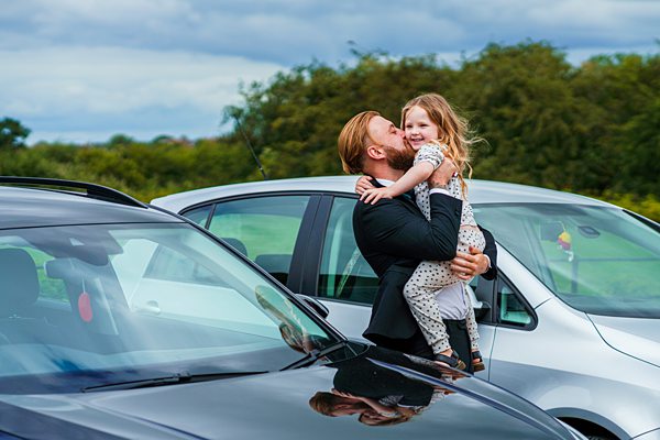 Father kissing happy daughter near cars in car park.