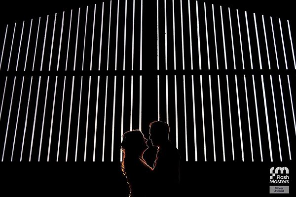 Couple silhouetted against illuminated vertical lines at night.