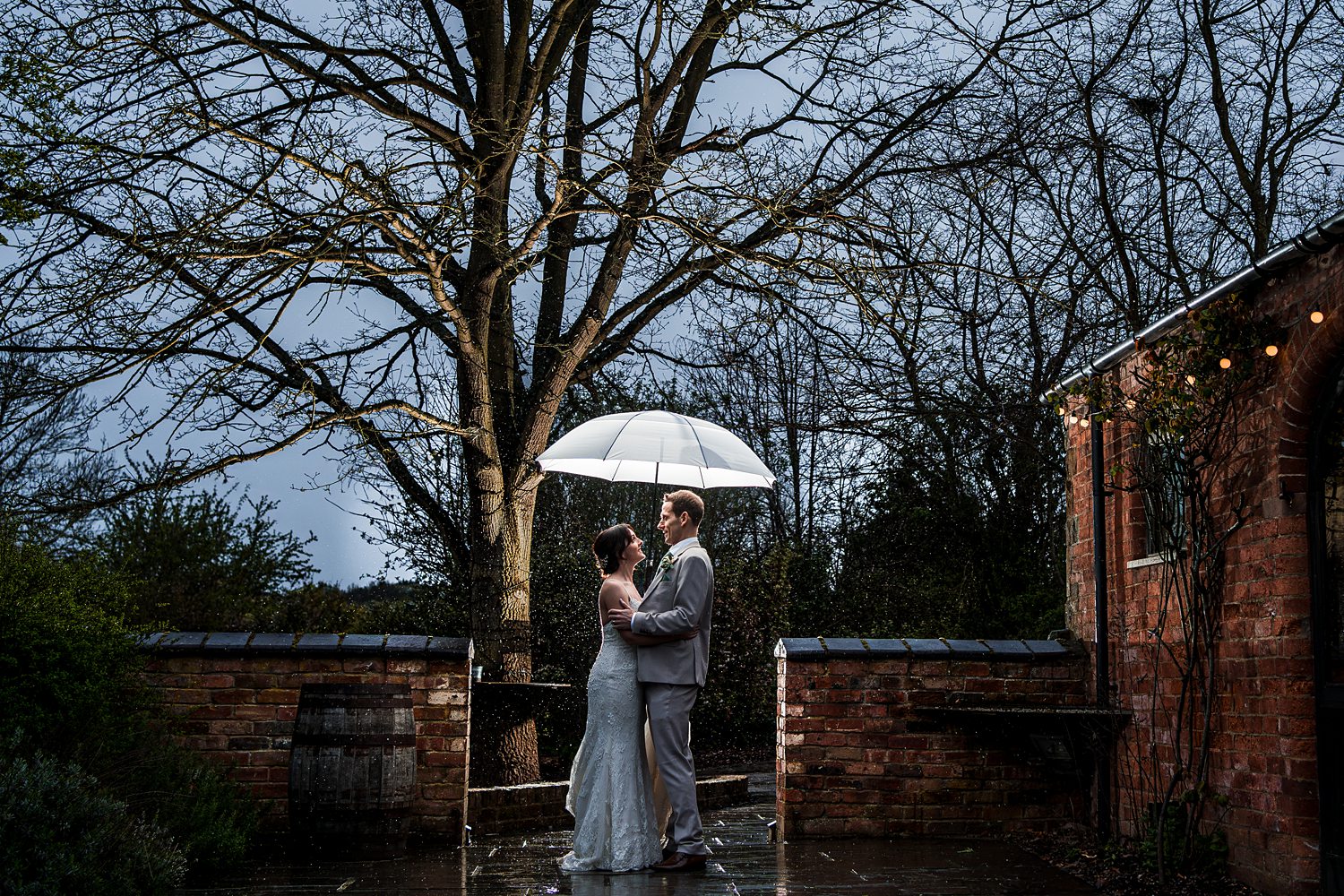 Couple with umbrella in romantic rainy wedding scene.