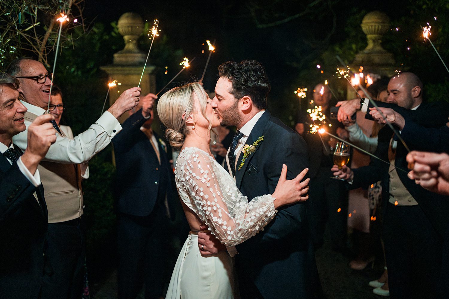 Couple kissing amid sparkler celebration at night wedding.
