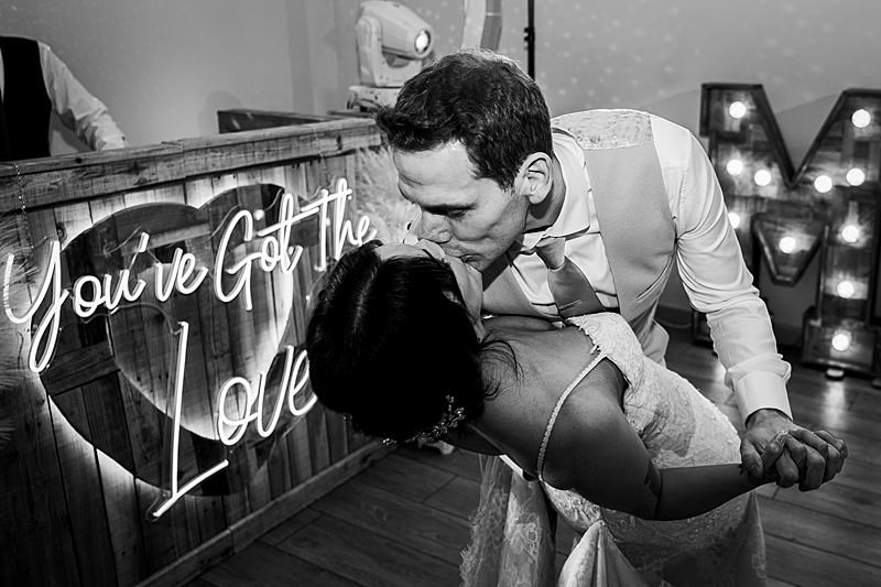 Couple kissing at wedding, romantic sign in background.