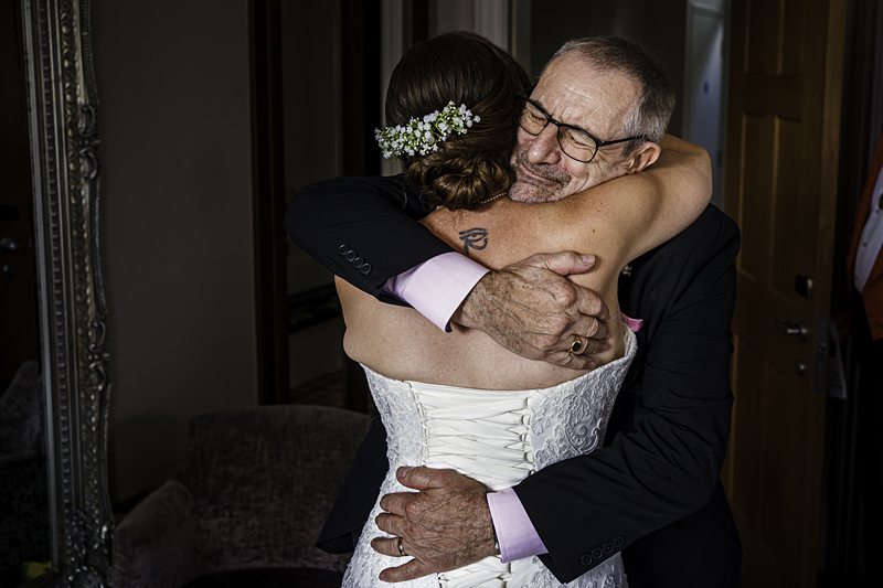 Bride hugs father affectionately before wedding ceremony.