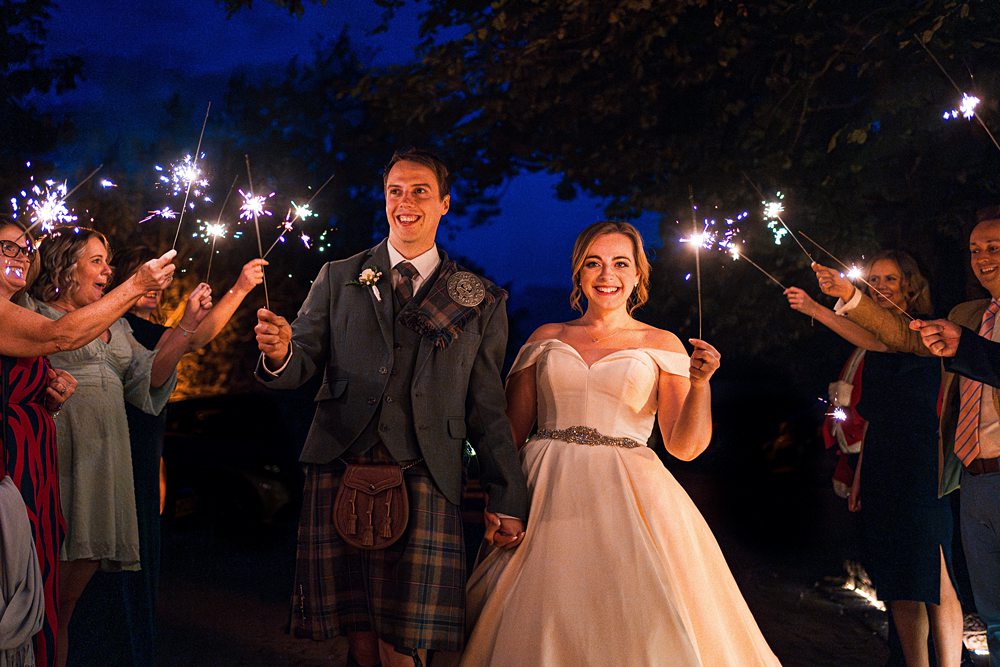 Bride and groom with sparklers surrounded by guests.