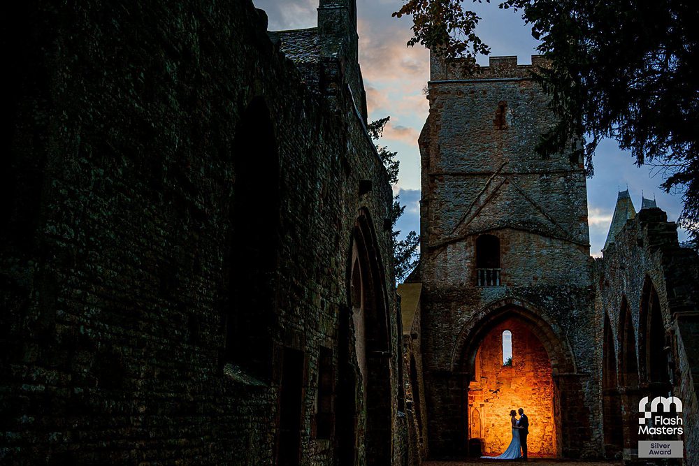 Couple silhouette in illuminated church ruins at sunset.