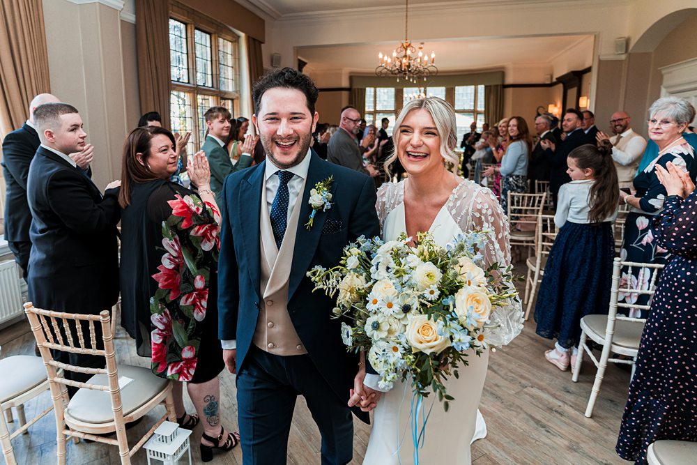Happy couple walking down wedding aisle, smiling guests.