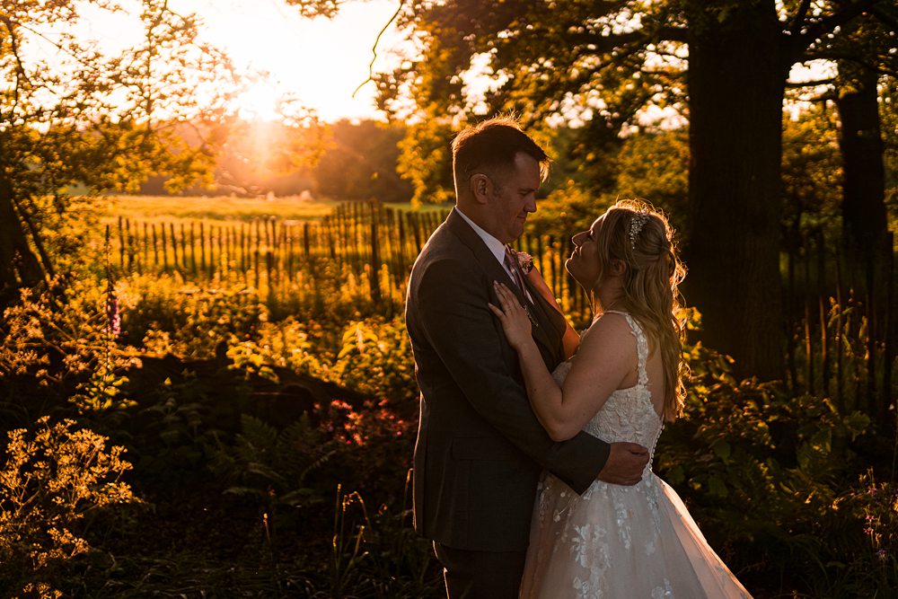 Bride and groom embrace at sunset in garden.