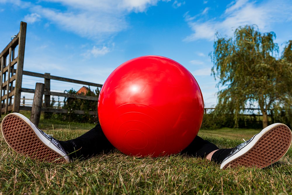 Person hidden behind large red ball outdoors.