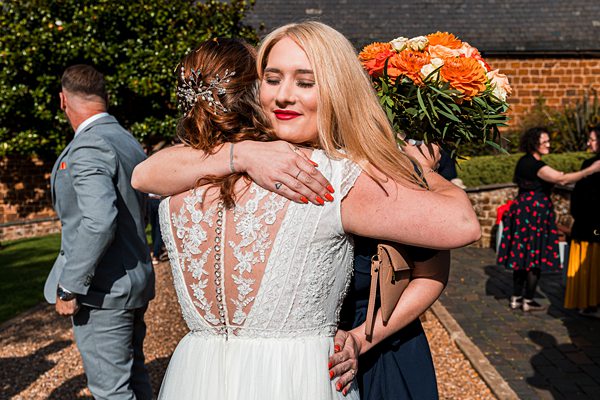 Two women embrace at a sunny outdoor wedding.