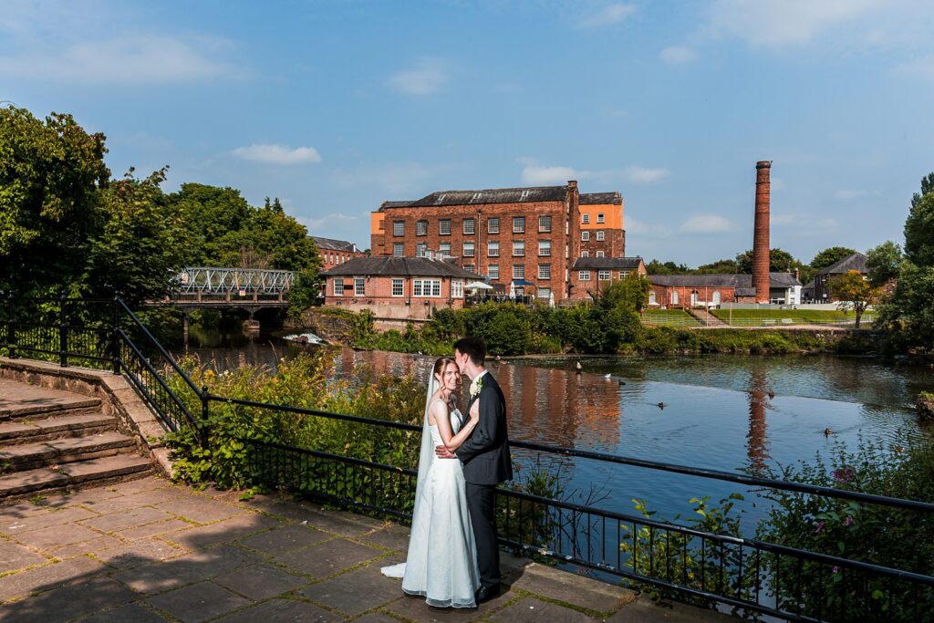 Bride and groom by a riverside mill building.