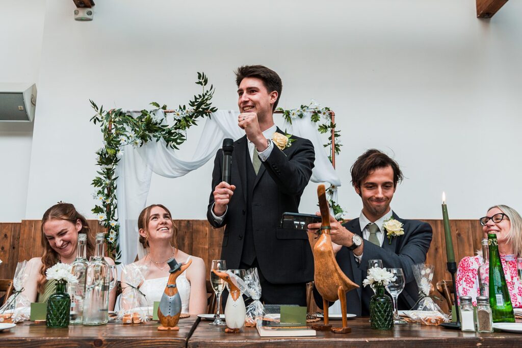 Groom giving a speech at wedding reception table.