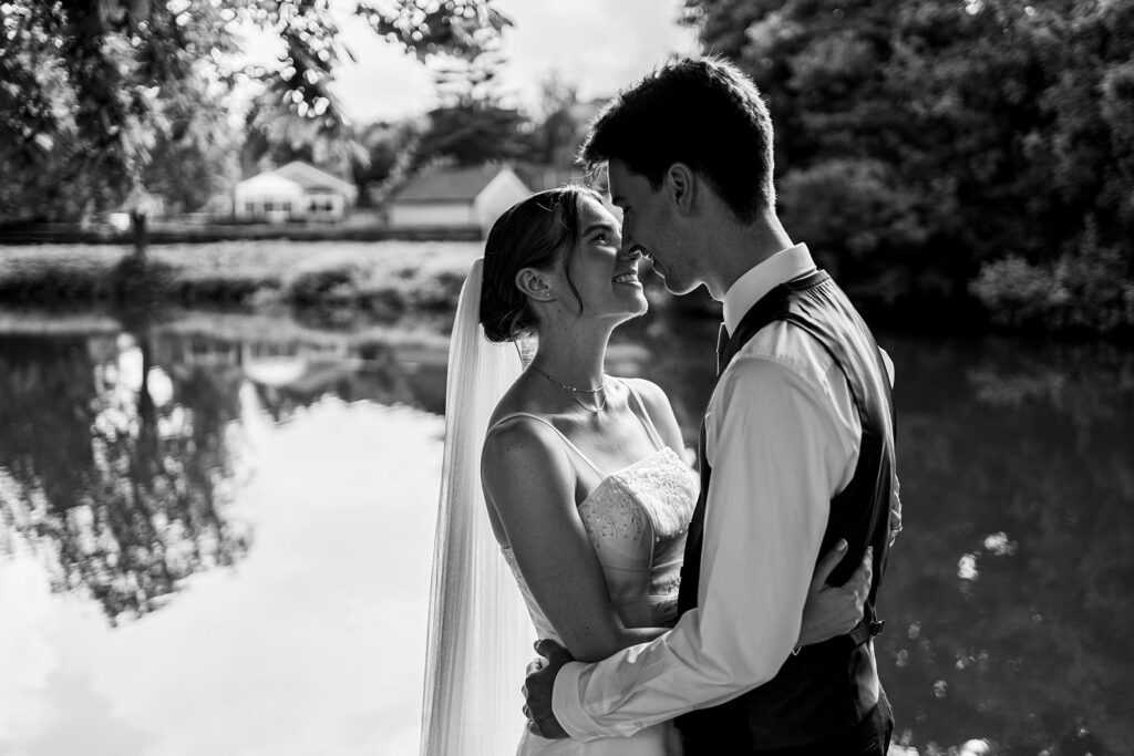 Bride and groom embrace by lakeside
