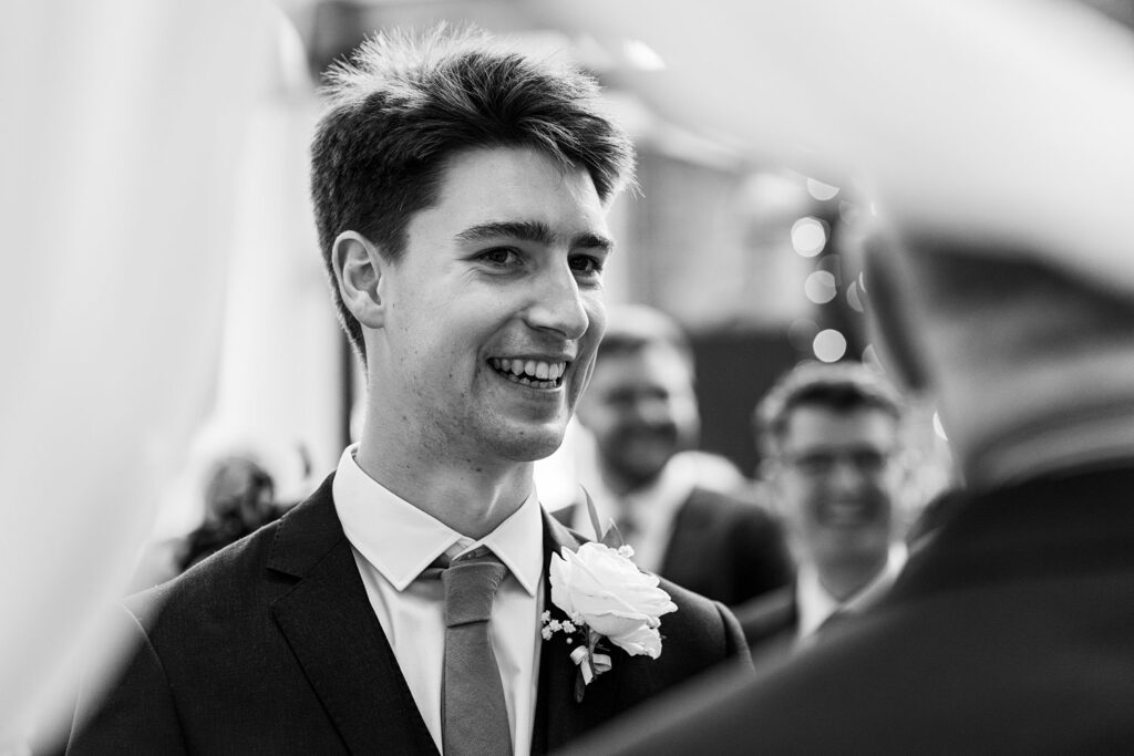 Smiling groom at wedding ceremony, wearing suit and boutonnière.
