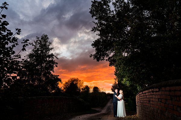 Couple embracing under vibrant sunset sky on bridge.
