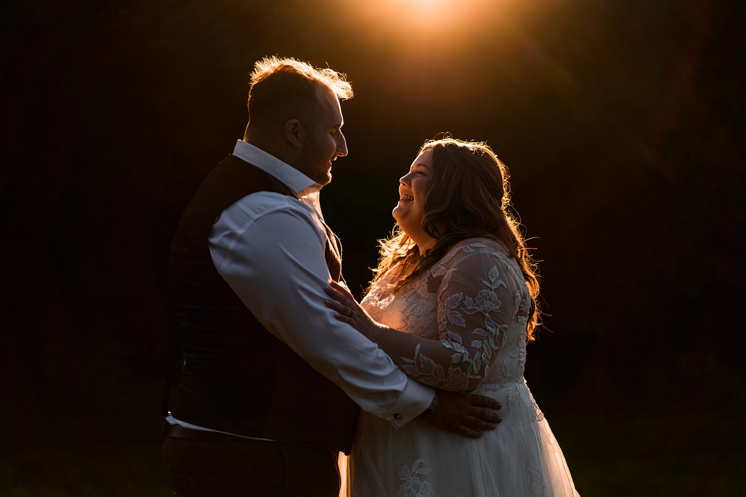 Couple embracing at sunset in wedding attire.