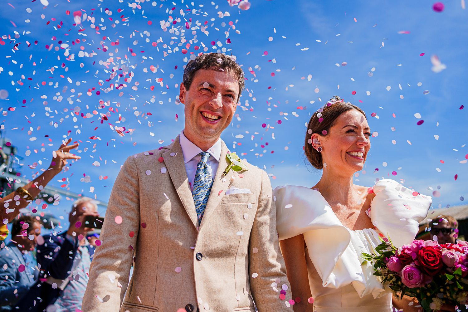 Smiling couple under confetti at outdoor wedding.