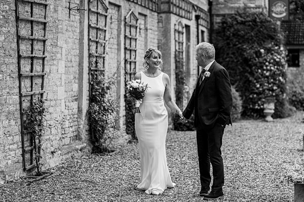 Bride and groom holding hands, walking outside building.