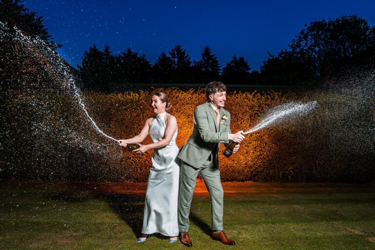 Couple joyfully spraying champagne outdoors at night.