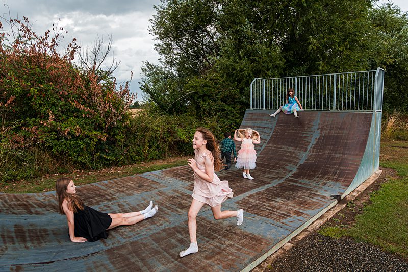 Children playing on outdoor skate ramp in dresses.