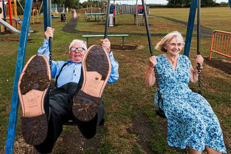 Elderly couple joyfully swinging in playground